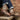 Brown and white sneakers with striped design worn by a person sitting on a wooden bench against a brick wall.