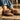 Brown sneakers with striped design worn by a person on a stone pavement.